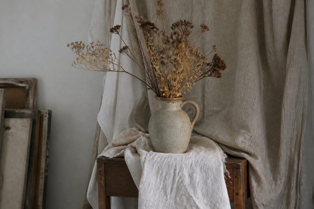 Still-life jug with dried flowers and linen drapery on a wooden stand